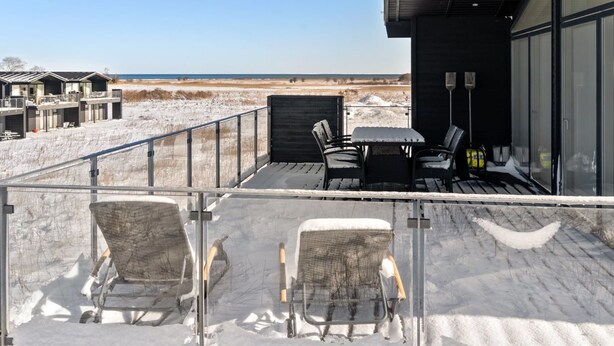 Een modern gebouw met een balkon dat uitkijkt over een besneeerd landschap en een strand.