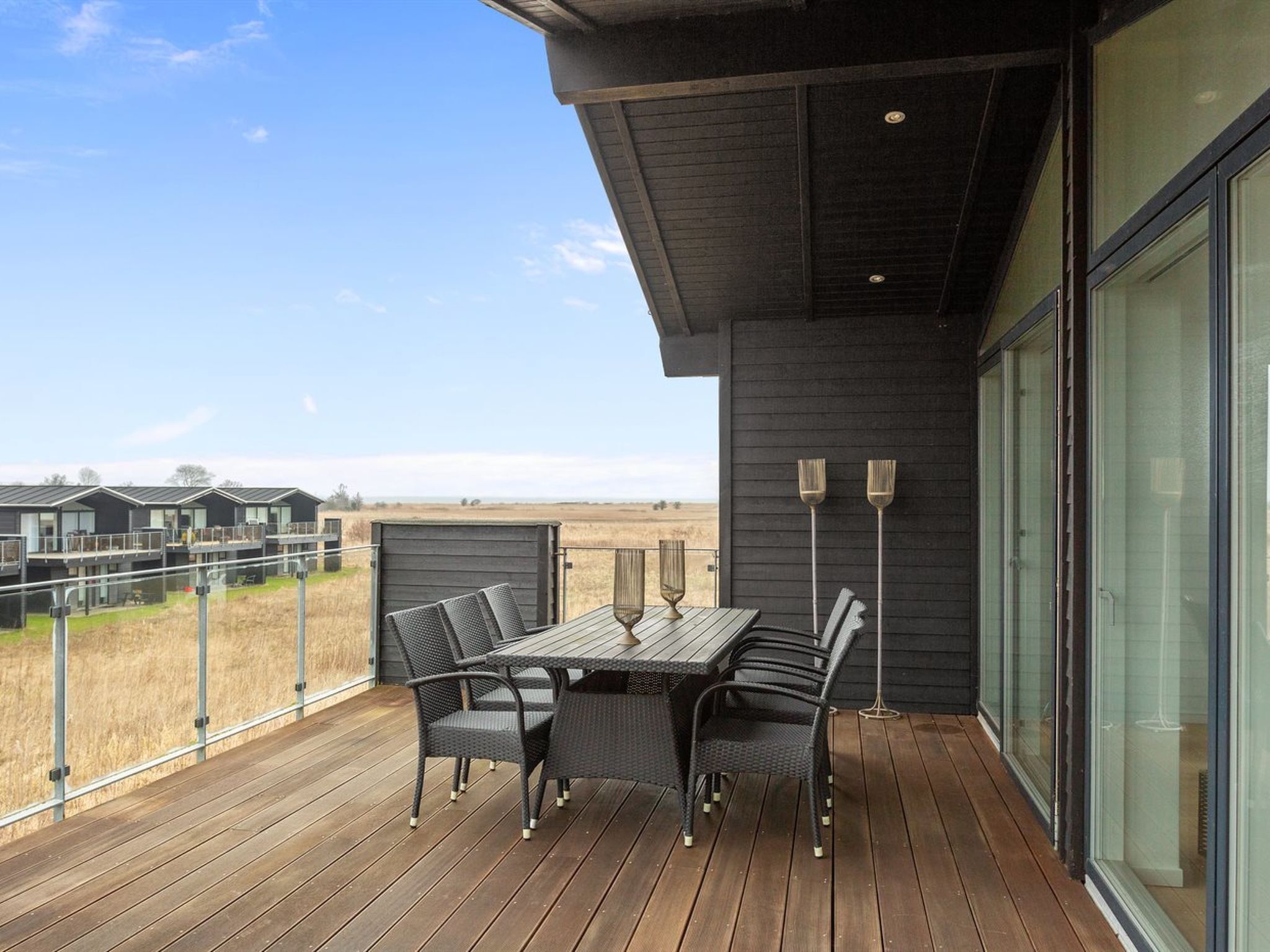 A modern outdoor deck with a table and chairs, overlooking a field.