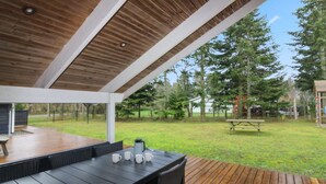 An outdoor patio with a wooden deck, a black table with chairs, and a view of a grassy area with trees and a house in the background. - "Acucena" - 1.3km from the sea by Interhome (Bindslev)