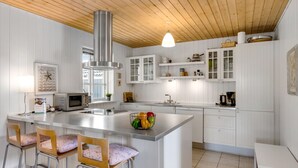 Une cuisine moderne avec des meubles blancs, un îlot central doté de tabourets de bar, une hotte de cuisine en acier inoxydable et un luminaire suspendu.