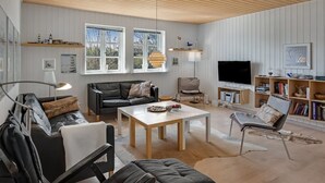 Un salon moderne avec un canapé, une table basse et un téléviseur. On y trouve des fenêtres, des étagères et un plafond avec des poutres en bois.