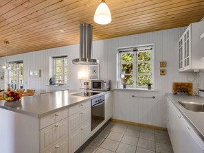 Una cocina moderna con armarios blancos, una isla central, una campana extractora de acero inoxidable y un ventanal con vistas a árboles.