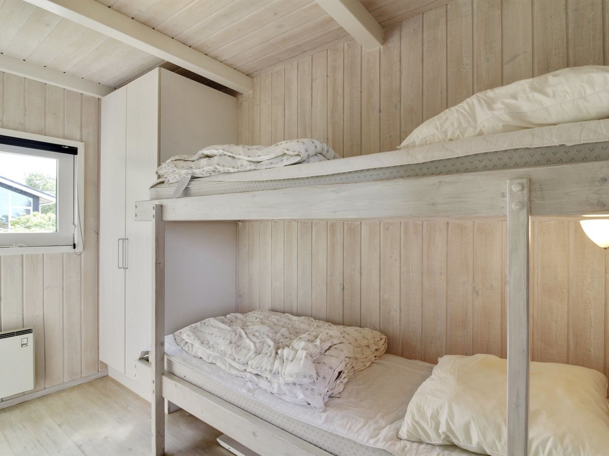 Une chambre avec un lit superposé, une fenêtre, des murs en bois et un radiateur.
