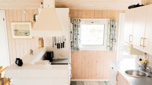 A compact kitchen with wooden walls, a window with floral curtains, and a small island with a sink and countertop. - "Mila" - 750m from the sea by Interhome (Bindslev)
