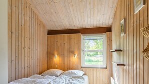 A bedroom with a wooden slat ceiling, a bed with white bedding, two wall-mounted lights, and a window with a view of greenery. - "Menka" - 1.3km from the sea by Interhome (Bindslev)