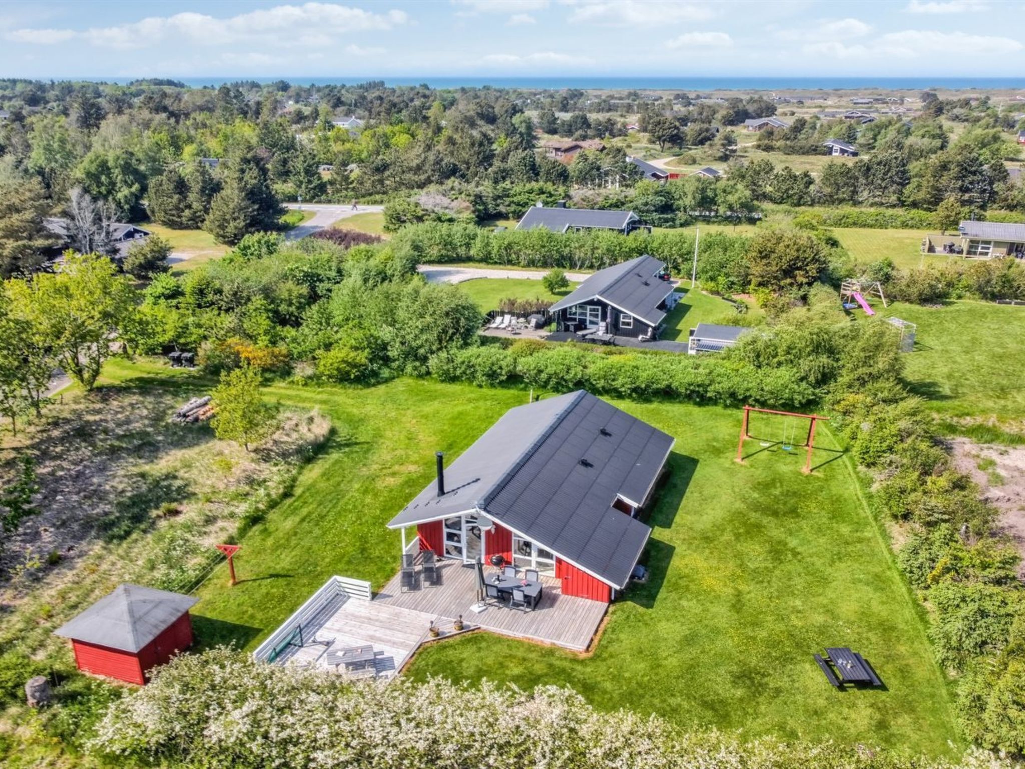A large house with a deck and a swimming pool, surrounded by lush greenery and other houses.