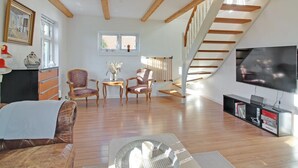 Ein geräumiger Loft mit freiliegenden Holzbalken, einer Treppe, einem großen Fernseher und einer gemütlichen Sitzecke mit gemusterten Stühlen.