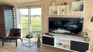 A modern living room with a large flat-screen TV, wooden flooring, a cozy chair, and a large window offering a view of the outdoors. - "Hinda" - 1.2km from the sea by Interhome (Bindslev)