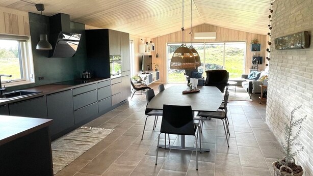 A modern kitchen with dark cabinetry, a large island, and a dining area with a round table and chairs. - "Hinda" - 1.2km from the sea by Interhome (Bindslev)