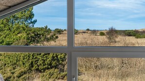A room with a large window offering a view of a dry, grassy landscape with sparse trees and a clear sky. - "Riika" - 425m from the sea by Interhome (Hirtshals)