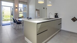 Une cuisine moderne dotée d’un grand îlot central, de luminaires suspendus et offrant une vue sur l’extérieur.