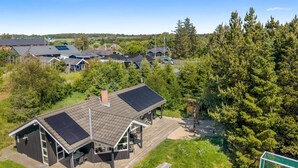 Een huis met een groot terras, zonnepanelen op het dak en een omliggend bebost gebied.
