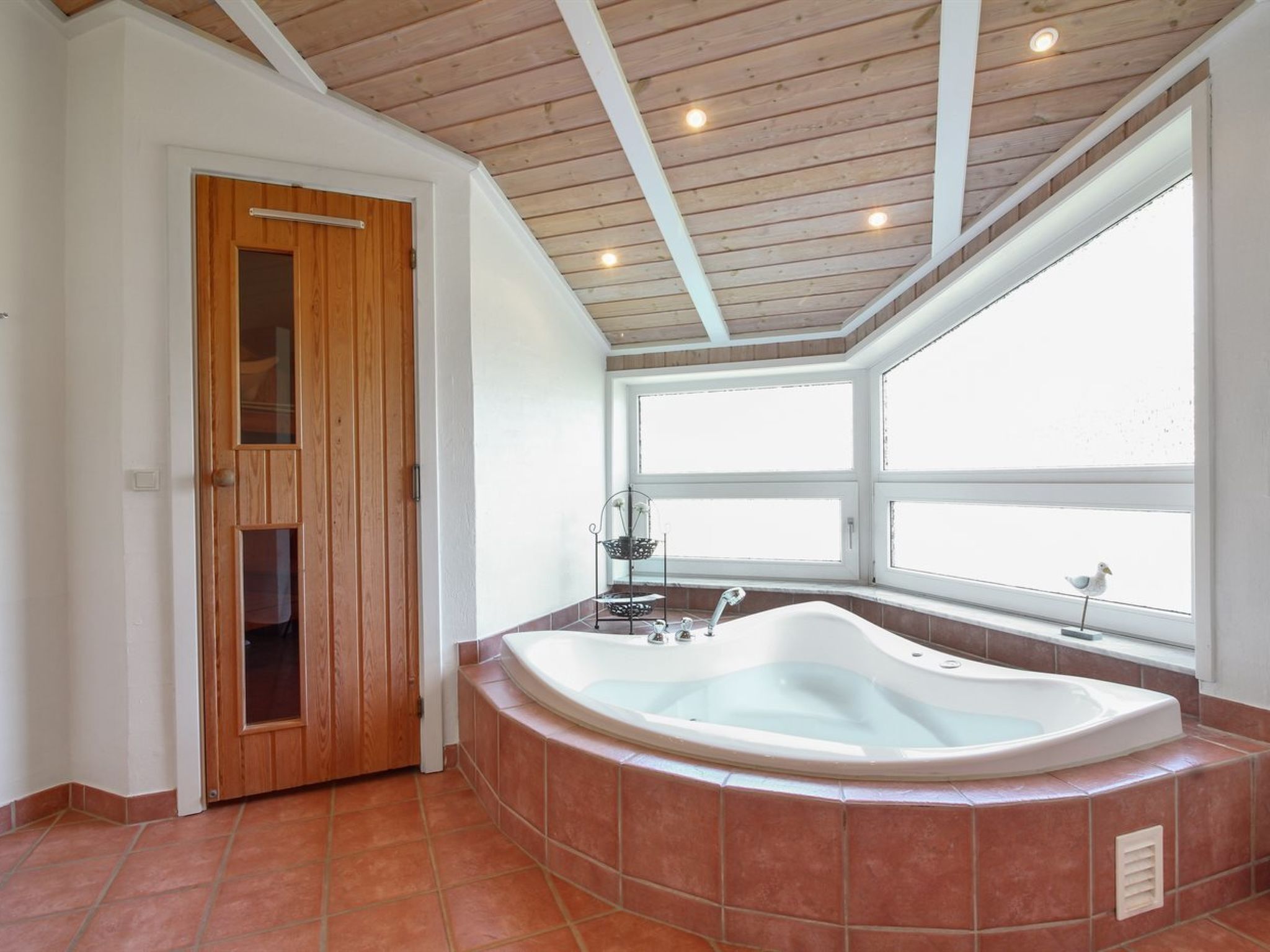Un baño con puerta de madera, una bañera independiente y un ventanal que proporciona luz natural.