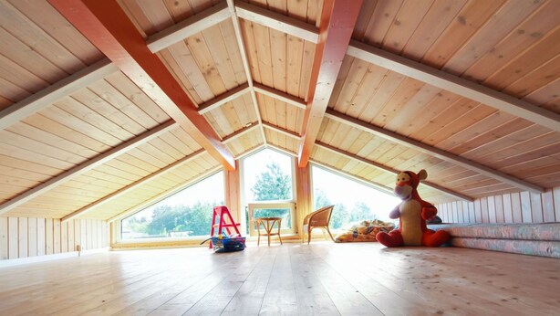Amplia habitación en ático con vigas de madera, un ventanal grande y una silla roja.