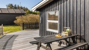 Eine Holzterrasse mit einem Picknicktisch, ein kleines Gebäude mit einem Fenster und ein Zaun im Hintergrund.