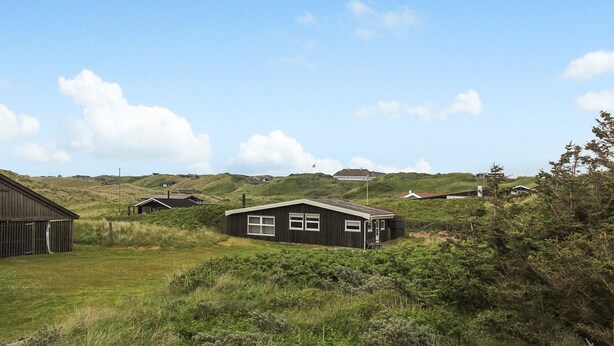 A rural landscape with a small, dark-colored house surrounded by greenery and hills.