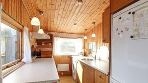 A compact kitchen with wooden walls, a refrigerator, a sink, and a window with curtains.
