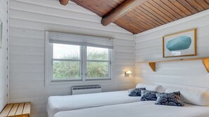 Ein Schlafzimmer mit zwei Betten, einem Fenster, einer Wandleuchte und einem Gemälde.