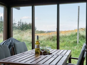 Une table en bois, avec une bouteille de vin et des verres, placée devant un champ verdoyant et un ciel dégagé.