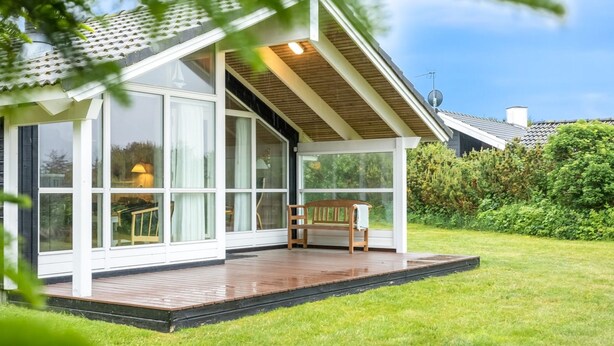 Een modern huis met grote ramen, een houten terras en een tuin.