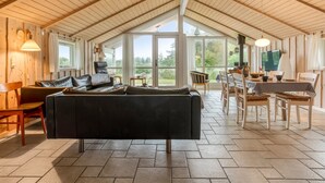 Een ruime woonkamer met een hoge plafond, een open haard en een eethoek met een tafel en stoelen.