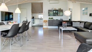 Amplia sala de estar con una mesa de comedor, sofá de cuero negro y una cocina al fondo.