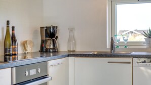 Una cocina con cafetera, dos botellas de vino, un florero y una ventana con vistas.