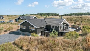 Una casa moderna con una amplia terraza, rodeada de paisaje natural y otras viviendas similares.
