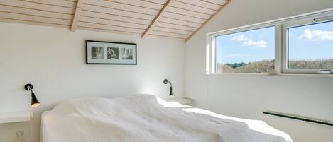 A bedroom with a wooden ceiling, a bed with a white bedspread, a picture on the wall, and a window with a view of trees.