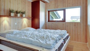 Een slaapkamer met een bed, houten wanden, een raam en een plank met planten.