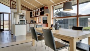 Een moderne keuken met houten balken, een centraal eiland en een eethoek met een grote tafel en stoelen.