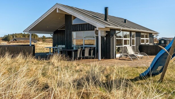 Ein modernes Haus mit einer großen Terrasse, einem überdachten Sitzbereich im Freien und Blick auf die umliegende Landschaft.