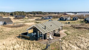 Ein modernes Haus mit einer großen Terrasse, umgeben von offenen Feldern und einigen anderen Häusern.