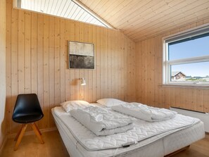 Ein Schlafzimmer mit Holzboden, einem Bett mit weißer Bettwäsche, einem schwarzen Stuhl und einem Fenster mit Blick auf Gebäude.