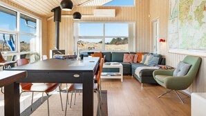 Ein modernes Interieur mit Holzbalkendecke, großen Fenstern, einem Essbereich, einer Couch und einer Weltkarte an der Wand.