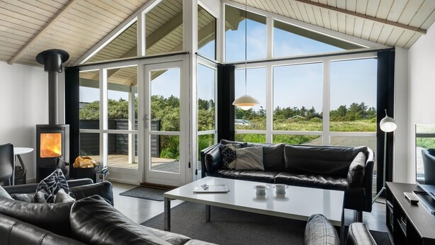 Een moderne woonkamer met een open haard, leren bank en grote ramen met uitzicht op de omgeving.