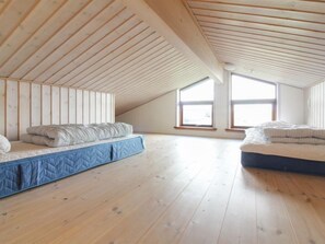 Two beds are positioned in this cozy attic space with a sloping ceiling, offering a view of the outside through large windows.