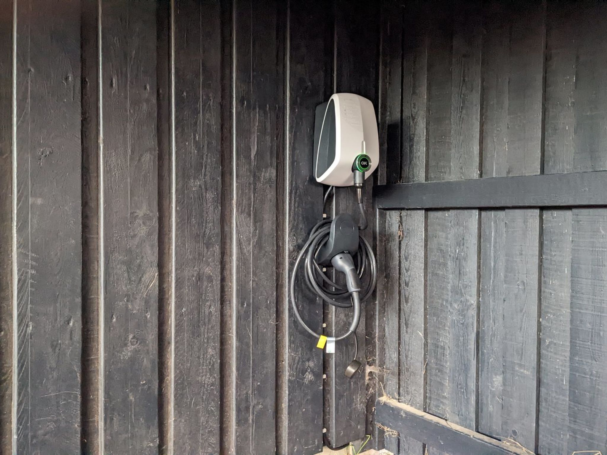 Un enchufe eléctrico fijado a la pared, un cable enrollado y una etiqueta amarilla.