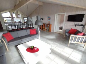 Relax in this stylish living space with a high ceiling and exposed beams, featuring a comfortable sofa, armchair, and bookshelf.