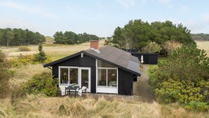 A modern house with a large glass door, a small patio with a table and chairs, surrounded by natural landscape.
