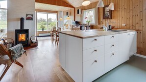 A modern kitchen with a central island, wooden ceiling, and large windows.