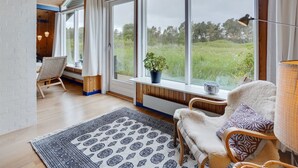 A cozy room with large windows, a wooden ceiling, and a view of a grassy field.