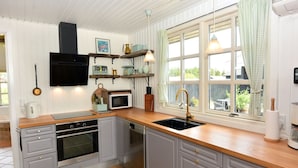 Eine Küche mit grauen Schränken, einer Holz Arbeitsplatte, einem schwarzen Spülbecken und einem Fenster mit Vorhängen.