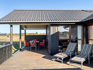 Un espacio al aire libre cubierto con una terraza de madera, una mesa con sillas y sillones.