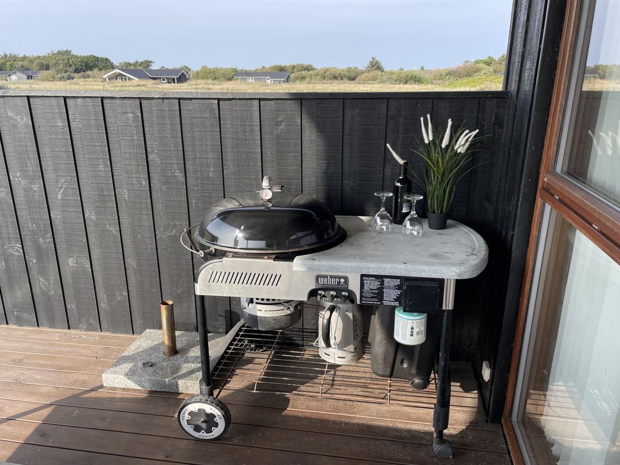 A portable grill with a control panel, a pot, and a water container on a wooden deck.