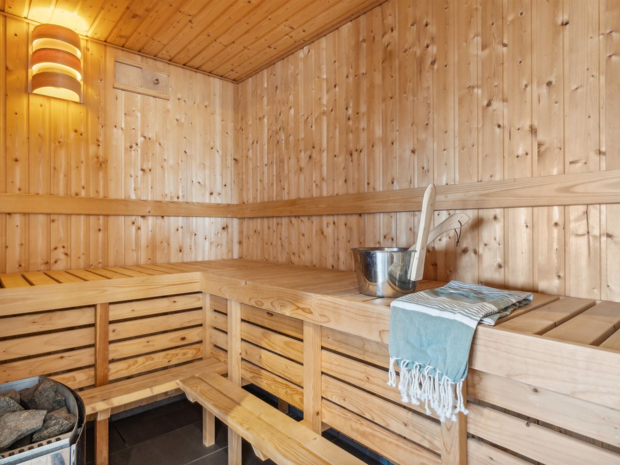 Un sauna en bois avec des bancs, un seau en métal et une cuillère en bois.
