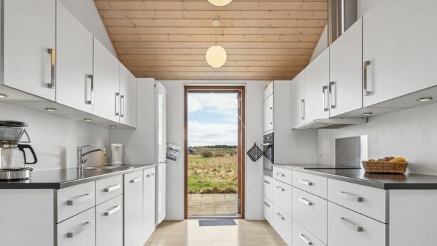 Une cuisine moderne avec des armoires blanches, un plafond en bois et une vue sur l’extérieur.
