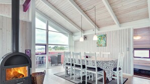 Un cuarto acogedor con una estufa de leña, una mesa de comedor con sillas y un amplio ventanal con vistas al exterior.