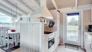 Una cocina moderna con armarios blancos, un comedor con mesa y sillas, y vistas al exterior a través de un ventanal.