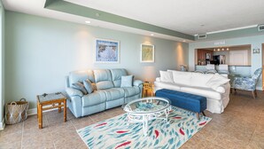 Un salon avec un canapé bleu, un canapé blanc, une table basse en verre et un tapis à motifs.